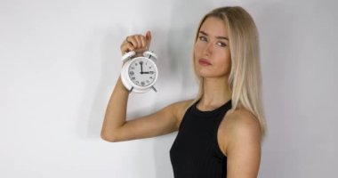 An attractive blonde haired woman holding up an old style alarm clock that is set to 3 o'clock, waking up at 3am or 3pm concept, filmed in 8k footage