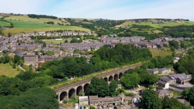 Aerial drone footage of a scenic view of the village of Slaithwaite in the town of Huddersfield in the UK taken with a drone on a hot sunny summers day, showing housing estates and train tracks.