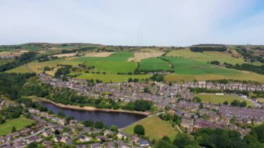 Aerial drone footage of a scenic view of the village of Slaithwaite in the town of Huddersfield in the UK taken with a drone on a hot sunny summers day, showing housing estates and train tracks.