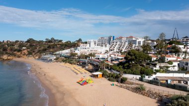 Portekiz 'in Albufeira şehrindeki Albufeira şehrinin havadan çekilmiş fotoğrafı Praia da Oura altın kumlu plajını gösteriyor, şehirde oteller ve apartmanlar var, yaz günlerinde çekilmiş..