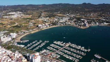 İspanya 'nın Balear Adaları' ndaki İbiza adasındaki Sant Antoni köyündeki bir kumsalın insansız hava aracı görüntüleri kayık limanını ve Playa de San Antonio, İbiza olarak bilinen plajı gösteriyor.