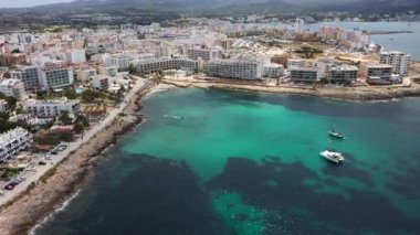 Ibiza Spains Balearic Adaları 'nın batı kıyısındaki Sant Antoni de Portmany kasabasının insansız hava aracı görüntüleri okyanus cephesini ve Cal des Moro sahilini okyanusta teknelerle gösteriyor.