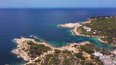 İspanya 'nın Balear Adaları' ndaki İbiza adasındaki Sant Antoni köyündeki Cala Graci adlı bir plajın insansız hava aracı görüntüleri, yaz mevsiminde okyanus manzarasını ve sahil cephesini gösteriyor..