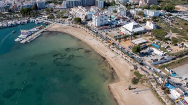 İspanya 'nın Balear Adaları' ndaki İbiza adasındaki Sant Antoni de Portmany kasabasındaki bir kumsalın insansız hava aracı fotoğrafı tekne limanını ve Playa de San Antonio olarak bilinen plajı gösteriyor.