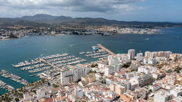 İspanya 'nın Balear Adaları' ndaki İbiza adasındaki Sant Antoni de Portmany kasabasındaki bir kumsalın insansız hava aracı fotoğrafı, oteller ve daireli tekne limanını ve limanı gösteriyor.