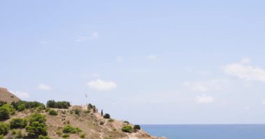 İspanya 'nın güzel Benidorm şehrinin Cala Almedraba sahilindeki yamaçta rüzgarda dalgalanan bir İspanyol bayrağını gösteren görüntüsü..