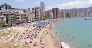 Benidorm İspanya, 1 Temmuz 2023: İspanya 'nın güzel Benidorm şehrinin sahili kalabalık Cala del Mal Pas plajını, plajda dinlenen ve güneşlenen insanları gösteriyor.