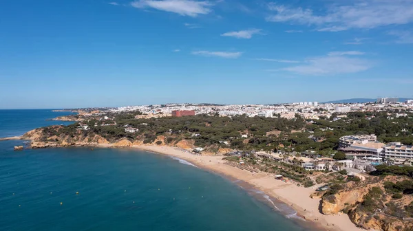 Portekiz 'in Albufeira şehrindeki Albufeira şehrinin havadan çekilmiş fotoğrafı Praia da Oura altın kumlu plajını gösteriyor, şehirde oteller ve apartmanlar var, yaz günlerinde çekilmiş..