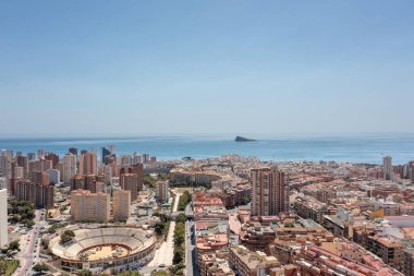 İspanya 'daki Benidorm kasabasının havadan çekilmiş fotoğrafı, şehirdeki bina ve daireleri ve arka planda okyanus bulunan Plaza De Toros Benidorm olarak bilinen eski tarihi boğa güreşi ringini gösteriyor.