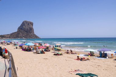 Calpe, Alicante, 5 Temmuz 2024: İspanya 'nın güzel şehri Calpe' nin yaz mevsiminde turistler ve yerel halkla birlikte kumsalda güneşli havanın keyfini çıkarırken çekilmiş fotoğrafı