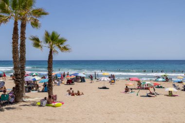 Calpe, Alicante, 5 Temmuz 2024: İspanya 'nın güzel şehri Calpe' nin yaz mevsiminde turistler ve yerel halkla birlikte kumsalda güneşli havanın keyfini çıkarırken çekilmiş fotoğrafı