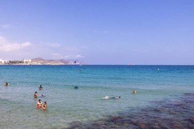 Villajoyosa, İspanya 15 Temmuz 2024: Güneşli bir yaz gününde kumlu plajda ve okyanusta turistleri gösteren güzel Villajoyosa köyünün fotoğrafı