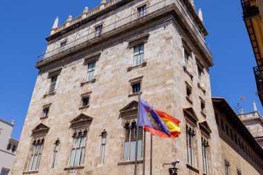 İspanya 'nın Alicante kentindeki Valencia kasabasında güneşli bir günde İspanya' nın AB ve Valensiya Topluluğu bayrağını gösteren sarı bir binada bulunan 3 İspanyol bayraklarından oluşan bir fotoğraf.
