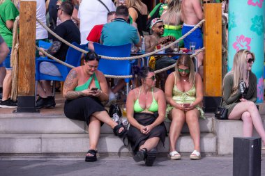 Benidorm İspanya, 17 Mart 2024: İspanya 'da Benidorm' da çekilen fotoğraf, güneşli bir yaz gününde plaj cephesinde Aziz Patrick Günü 'nü kutlayan insanları gösteriyor..