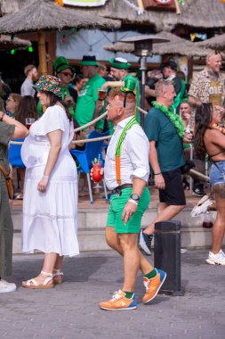 Benidorm İspanya, 17 Mart 2024: İspanya 'da Benidorm' da çekilen fotoğraf, güneşli bir yaz gününde plaj cephesinde Aziz Patrick Günü 'nü kutlayan insanları gösteriyor..