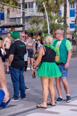 Benidorm İspanya, 17 Mart 2024: İspanya 'da Benidorm' da çekilen fotoğraf, güneşli bir yaz gününde plaj cephesinde Aziz Patrick Günü 'nü kutlayan insanları gösteriyor..