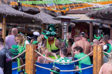 Benidorm İspanya, 17 Mart 2024: İspanya 'da Benidorm' da çekilen fotoğraf, güneşli bir yaz gününde plaj cephesinde Aziz Patrick Günü 'nü kutlayan insanları gösteriyor..
