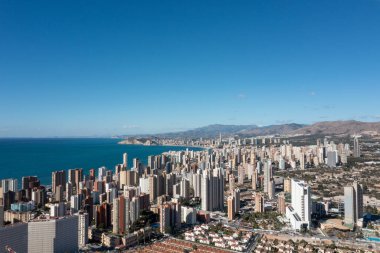 Yazın güneşli bir günde İspanya 'nın Benidorm şehrinin, yüksek katlı daireleri otelleri ve sahile ve okyanusa giden ana yolu gösteren insansız hava aracı fotoğrafı.