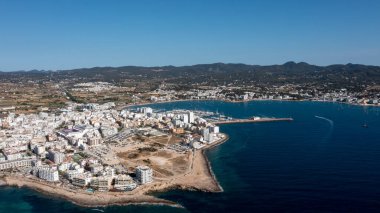 İspanya 'nın Balear Adaları' ndaki İbiza adasındaki Sant Antoni de Portmany kasabasındaki bir kumsalın insansız hava aracı fotoğrafı tekne limanını ve Playa de San Antonio olarak bilinen plajı gösteriyor.