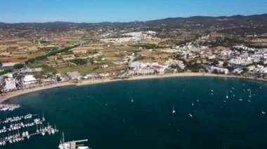 İspanya 'nın Balear Adaları' ndaki İbiza adasındaki Sant Antoni köyündeki bir kumsalın insansız hava aracı görüntüleri kayık limanını ve Playa de San Antonio, İbiza olarak bilinen plajı gösteriyor.