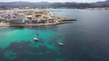 Ibiza Spains Balearic Adaları 'nın batı kıyısındaki Sant Antoni de Portmany kasabasının insansız hava aracı görüntüleri okyanus cephesini ve Cal des Moro sahilini okyanusta teknelerle gösteriyor.