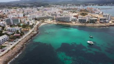 Ibiza Spains Balearic Adaları 'nın batı kıyısındaki Sant Antoni de Portmany kasabasının insansız hava aracı görüntüleri okyanus cephesini ve Cal des Moro sahilini okyanusta teknelerle gösteriyor.