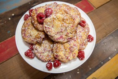 Mutfak masasında taze pişmiş ahududu ve beyaz çikolatalı kurabiyeler sergileniyor.