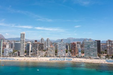 Yazın İspanya 'nın Benidorm şehrinin hava aracı fotoğrafı güneşli bir yaz gününde Playa de Levante plajını ve yüksek katlı apartman dairelerini ve otelleri gösteriyor.