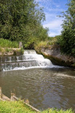 Photo of the beautiful town of Bedale, which is a market town and civil parish in North Yorkshire, England showing the Bedale Beck and waterfall on a hot sunny day in the summer time clipart