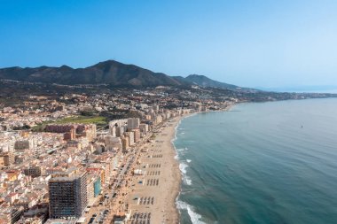 İspanya 'nın Malaga kıyı kasabası Fuengirola' nın önündeki güzel sahil insansız hava aracı fotoğrafı, arka planda dağlar olan kumlu sahil, oteller ve daireleri gösteriyor.