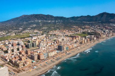 İspanya 'nın Malaga kıyı kasabası Fuengirola' nın önündeki güzel sahil insansız hava aracı fotoğrafı, arka planda dağlar olan kumlu sahil, oteller ve daireleri gösteriyor.