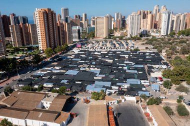 Aerial drone photo of the city of Benidorm in Spain in the summer time showing the famous outside market and market stalls with the car park and busy road along side the markets and apartments clipart