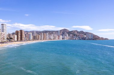 İspanya 'nın Benidorm şehrinin yazın çekilmiş fotoğrafı yüksek katlı daireleri ve Levante Sahili' nin yanındaki binaları ve arka plandaki montajları gösteriyor..