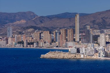 İspanya 'nın Benidorm şehrinin havadan çekilmiş fotoğrafı yüksek katlı daireleri ve Levante Sahili' nin yanındaki binaları ve arka plandaki tepeleri gösteriyor..