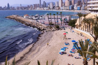 Benidorm İspanya, 14 Mart 2024: İspanya 'nın güzel Benidorm şehrinin fotoğrafı, Cala del Mal Pas plajında insanların plajda dinlendiğini ve yaz tatilinde güneşlendiklerini gösteriyor.