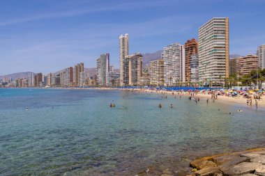 Photo of the beautiful city of Benidorm in Spain in the summer time showing high rise apartments and building along side the Levante Beach on a sunny day with people on the beach clipart