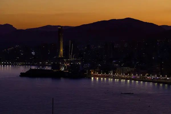 stock image Night time aerial photo of Benidorm Playa Levante beach in the evening showing the sun setting behind the mountains and the hotels and high rise apartments on the beach front