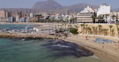 Güzel Benidorm kasabasının, yaz mevsiminin güneşli bir yaz gününde kumlu sahilde güneşlenen insanlarla dolu kayık limanında Cala del Mal Pas Plajı 'nı gösteren görüntüsü.