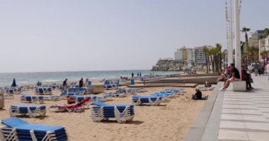 Benidorm İspanya, 15 Mart 2024: İspanya 'nın Benidorm kentinin yazın çekilmiş görüntüleri Levante Sahili boyunca turistlerin ve plajda insanların yürüdüğü yolları gösteriyor