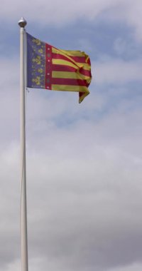 Açık bir günde rüzgarda sallanan Valensiyalı topluluk bayrağının ağır çekimde çekilmiş bir portre görüntüsü. Valencia Topluluğu İspanya 'nın özerk bir topluluğudur.