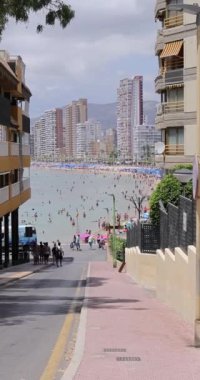 Benidorm İspanya, 1 Temmuz 2023: İspanya 'nın güzel Benidorm şehrinin plajdaki kalabalık Playa de Levante plajına doğru yürürken çekilmiş portre görüntüleri