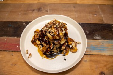 Nefis bir tabak Banoffee Pecan ve çikolatalı krep. Çikolata ve şeker kaynağına sarılı, ahşap mutfak masasında.