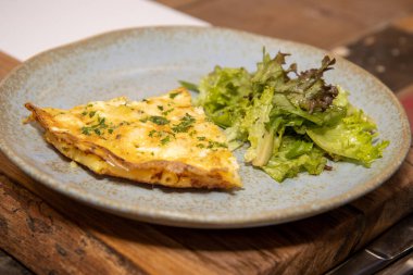 Mutfak masasına yerleştirilmiş gri tabakta peynirli makarna ve sebzeli frittata.