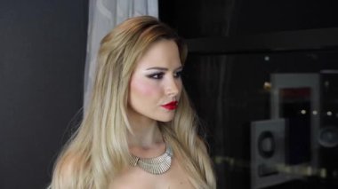 Uzun sarı saçlı, zarif ve çekici bir kadın. Canı sıkkın görünüyor. Dairesinin penceresinden dışarı bakıyor..