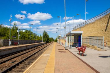 Wakefield West Yorkshire 'daki Castleford köyünde güneşli bir günde boş bir tren istasyonu, mavi gökyüzü ve gökyüzünde bulutlar olan İngiliz tren istasyonunu gösteriyor.