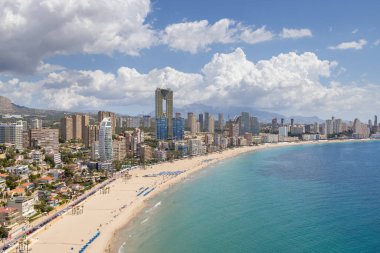 İspanya 'nın güzel Benidorm kasabasının hava aracı fotoğrafı güney sahilinde altın kumlu plajları ve güneşli bir yaz gününde gökyüzü ve birkaç bulutla birlikte daireleri gösteriyor.