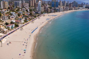 İspanya 'nın güzel Benidorm kasabasının hava aracı fotoğrafı güney sahilinde altın kumlu plajları ve güneşli bir yaz gününde gökyüzü ve birkaç bulutla birlikte daireleri gösteriyor.