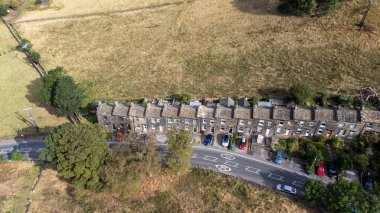 Aerial drone photo of the beautiful village of East Morton in Keighley in Yorkshire in the UK, showing old historic rows of traditional terraced houses by a road surrounded by farmers fields.