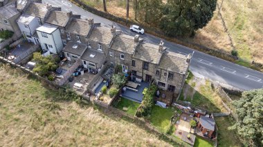 Aerial drone photo of the beautiful village of East Morton in Keighley in Yorkshire in the UK, showing old historic rows of traditional terraced houses by a road surrounded by farmers fields. clipart