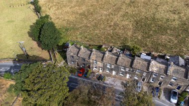 Aerial drone photo of the beautiful village of East Morton in Keighley in Yorkshire in the UK, showing old historic rows of traditional terraced houses by a road surrounded by farmers fields.